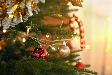 Christmas tree branch decorated with candy cane and baubles with blurred shiny lights on background
