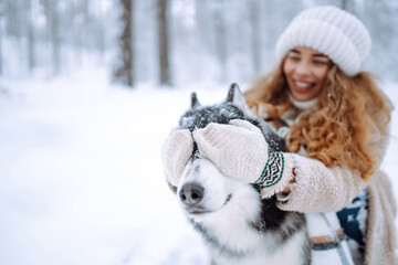 Beautiful young woman plays with her dog in the winter forest. First snow. Friendship, love and devotion concept. Outdoor recreation