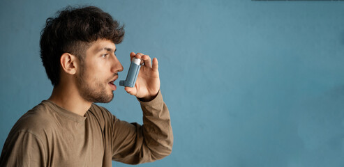 portrait of arabic young man using asthma inhaler against blue background at home