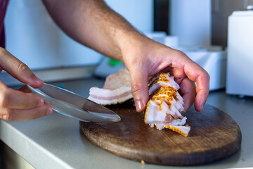 Use your hand to pick up thin pieces of chopped bacon on a cutting board and place them on a plate.