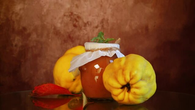 Ripe quince fruits with jam in a glass jar on a dark wooden table.