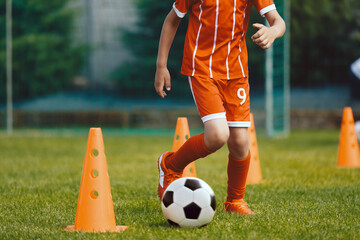 Obraz premium Children practicing dribbling at soccer pitch. Young boy running soccer ball in slalom drill between training cones