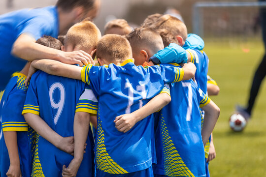 The soccer team huddles in a circle with a coach during the time break. Kids on the football team stand united and listen to the coach's motivational speech. Sporty children in blue soccer uniforms