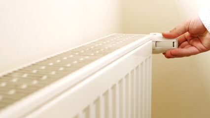 Unrecognizable man's hand check for heat and touch central heating system. White metal heating iron household radiator inside room. Budget in crisis concept. House in winter