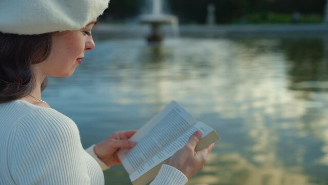 Attractive girl reading a book by a pond in Paris