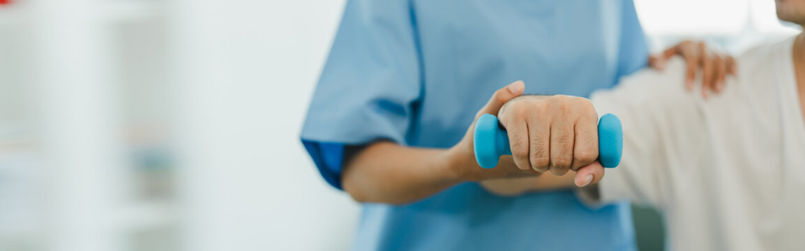 Physical therapist giving exercise by maintaining dumbbells on the arms and shoulders of a male patient. Physical therapy concept