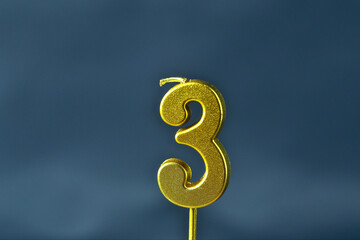 close up on gold number three birthday candle on a dark background.
