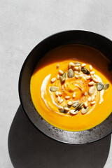 Seasonal autumn food. Pumpkin soup with cream, croutons and pumpkin seeds in a black plate on a gray background. Top view, copy space, minimalist