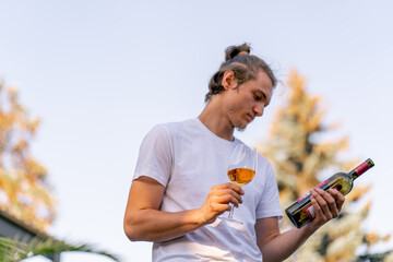 Naklejka premium Male professional sommelier prepares bottle of wine for tasting to guests in the winery garden