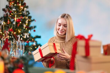 Obraz na płótnie Canvas A young woman holds a New Year's gift with a red ribbon in her hands. Close-up of a woman holding a Christmas gift box with a red ribbon. Holidays concept. A young girl in a white sweater holds a New