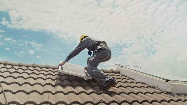 Low angle view of male worker holding solar panel while going on roof of clients house