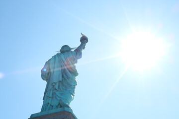 Statue of Liberty with sun shining in front on clear day