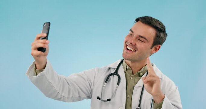 Selfie, happy man and doctor with stethoscope, pointing at picture and peace sign in studio. Photography, medical professional smile and hand gesture for telehealth isolated on a blue background.