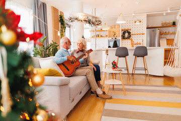 Senior couple playing the guitar and singing Christmas songs - obrazy, fototapety, plakaty