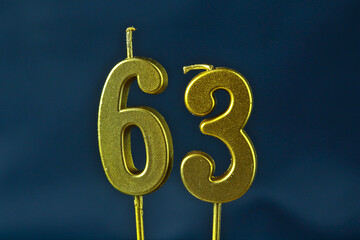 close up on the gold number sixty-third candle on a dark background.
