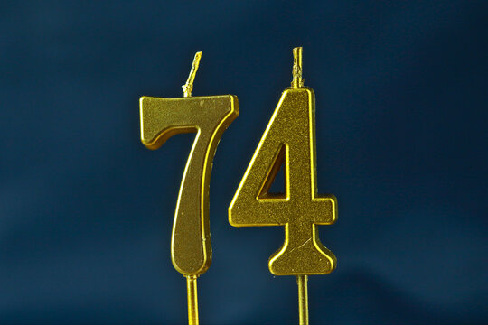 close up on the gold number seventy-fourth candle on a dark background.
