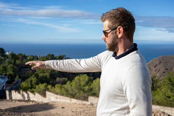 Portrait of handsome man wearing elegant white sweater and sunglasses, standing in the nature