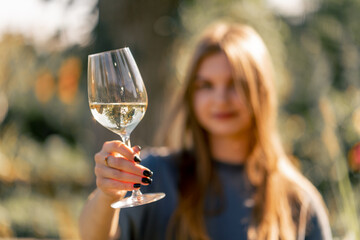 Portrait of a beautiful long-haired girl takes a sip of wine from a glass and hands it to the...