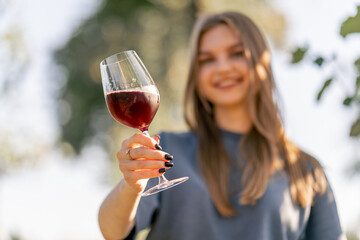 Portrait of a beautiful long-haired girl takes a sip of wine from a glass and hands it to the...