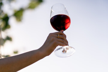 Close-up shot of a woman's hand in sunny garden holding a glass filled with aged red wine 