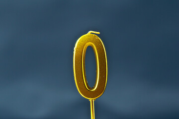 close up on gold number zero birthday candle on a dark background.
