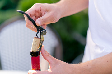 Close-up shot of a male sommelier's hand using a corkscrew to unscrew the wooden cork of wine bottle