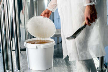 The hand of a technologist opens a barrel of natural liquid honey to be added to production of...
