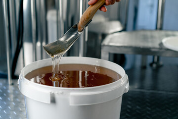 Close-up shot of a metal spoon stirring natural liquid honey which flows back into large bowl
