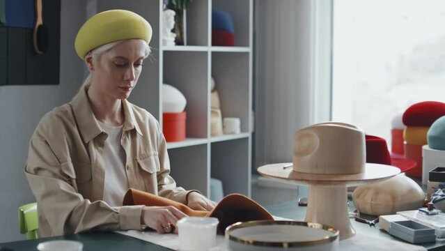 Medium shot of young Caucasian woman in millinery store turning hat inside out and coating it with felt stiffener
