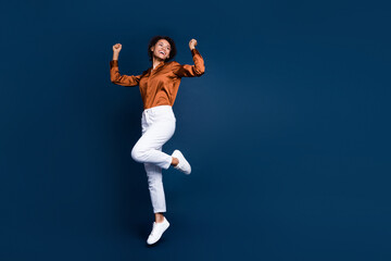 Fototapeta na wymiar Full size photo of attractive young woman jump celebrate win dressed stylish brown silk formalwear isolated on dark blue color background