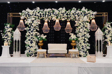 A beautiful decorated place for the wedding ceremony of the bride and groom in oriental style. Wedding arch made of white and blue fresh flowers. Beautiful decorative chandeliers and a white bench