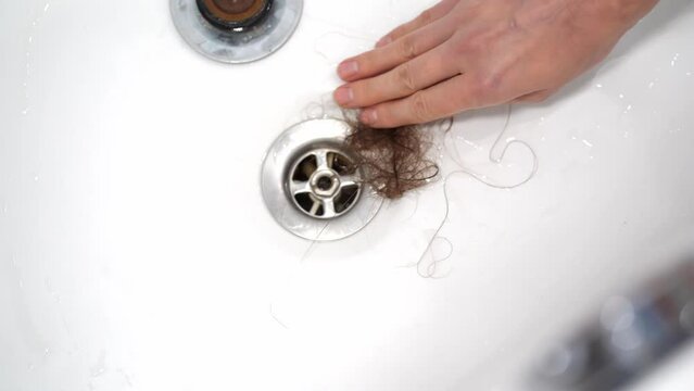 Cleaning the water drain in the sink from hair. A drain in the shower clogged with women's hair. The problem of hair loss and the problem of clogged plumbing. Clogged Drains.