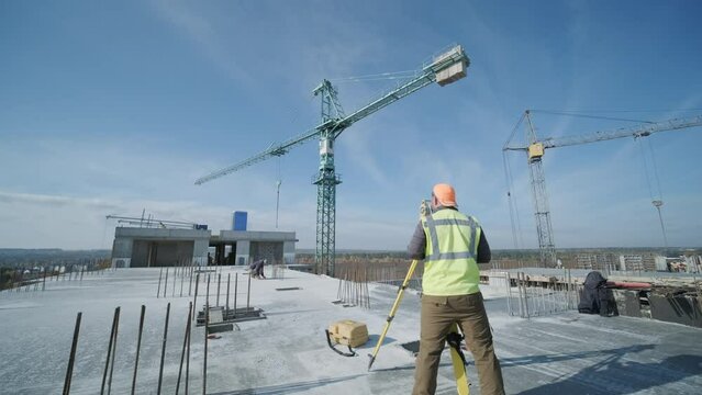 Geodetic works. Surveyor engineer in protective wear and red helmet using geodetic equipment at construction site. Professional equipment.