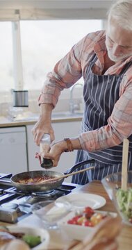Vertical video of senior caucasian man preparing dinner in kitchen, slow motion