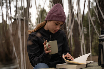 outside a Glamping , The smiling girl drinks coffee while reading a book on a wooden table outdoors...