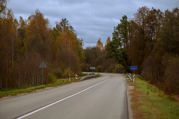 Colorful autumn landscape with asphalt road over the river through deciduous forest