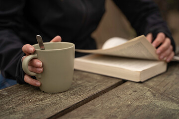 Glamping exterior, close-up detail of a woman's hands holding a cup of coffee while reading a book.
