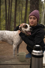 Girl wearing winter hat is sitting and petting her dog are outdoors
