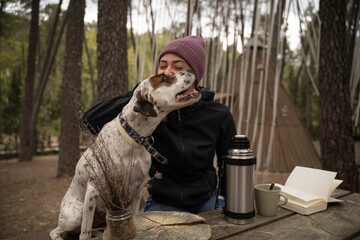 Girl wearing winter hat is sitting and petting her dog are outdoors
