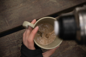 woman's hands pouring coffee on a wooden table in the open air.