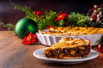 Obraz na płótnie Canvas Traditional British Christmas mince pie. Homemade sweet mincemeat cake, filled with spiced dried fruit, nuts and apples, on cozy wooden table with with Christmas tree and decoration