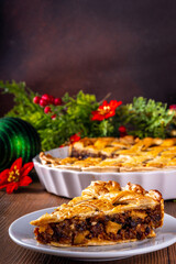 Traditional British Christmas mince pie. Homemade sweet mincemeat cake, filled with spiced dried fruit, nuts and apples, on cozy wooden table with  with Christmas tree and decoration