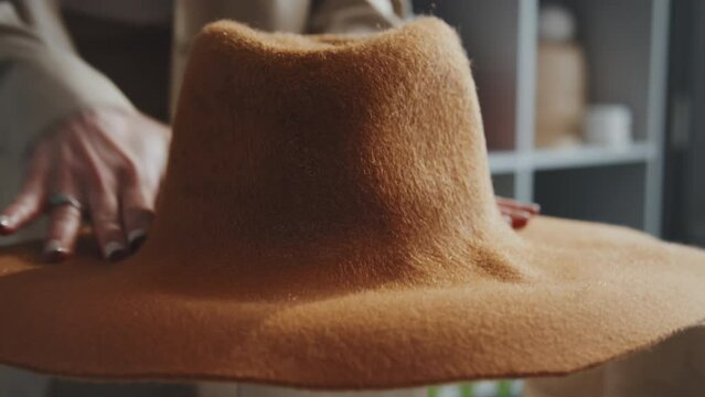 Selective focus close-up shot of unrecognizable Caucasian hat-maker flattening new oranger felt hat on mannequin