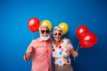 Portrait of a happy elderly couple with sunglasses wearing colorful shirts holding balloons