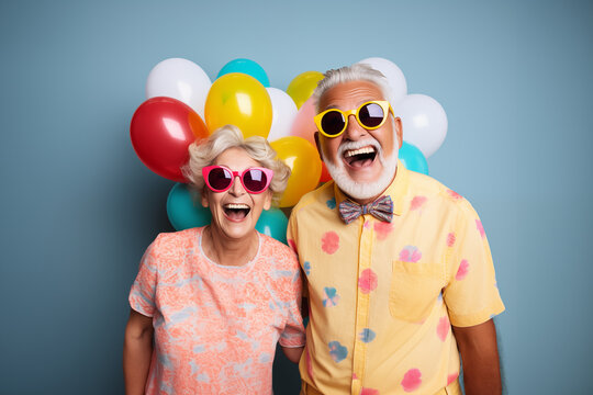 Portrait of a happy elderly couple with sunglasses wearing colorful shirts holding balloons