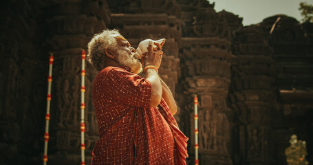 Authentic Shot of An Indian Senior Monk Blowing a Conch Shell in an Ancient Stone Temple. Elderly...