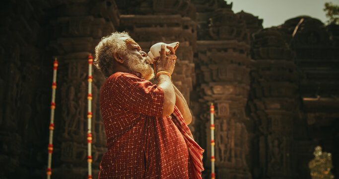 Authentic Shot of An Indian Senior Monk Blowing a Conch Shell in an Ancient Stone Temple. Elderly Man Performing Sacred Ritual on a Worship Day. Hinduism, South Asian Religion and Cultural Footage