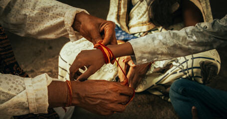 Close Up Authentic Footage of Hindu Priest Tying a Mauli Thread Around a Male Kid's Wrist in a Temple. Small Family Visiting Their Senior Guru, Seeking Guidance. Family Elder Passing on Wisdom - obrazy, fototapety, plakaty