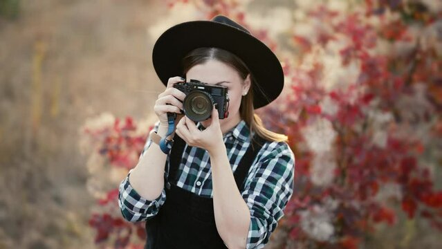 Young pretty woman takes pictures with DSLR camera outdoors on autumn background