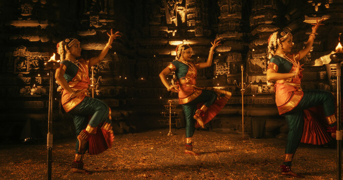 Portrait of Three Expressive Young Indian Dancers Performing Folk Dance Choreography Inside an Ancient Temple. Women in Traditional Clothes Dancing Bharatanatyam in Colourful Sari